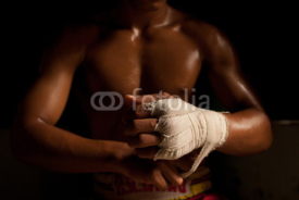 Naklejki The muscular fighter tying tape around his hand preparing to box
