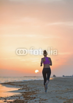 Fototapety Fitness young woman running on beach in the evening . rear view