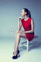 Naklejki young elegant woman in red dress sit on stool, studio shot