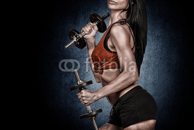 Athletic young woman doing workout with weights on dark backgrou