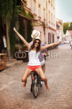 Fototapety Happy young woman riding on bicycle with her boyfriend
