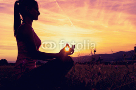 Naklejki Young athletic woman practicing yoga on a meadow at sunset, silhouette