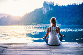 Naklejki Yoga lotus. Young woman doing yoga by the lake, sitting in lotus. 