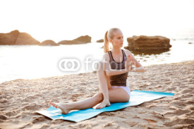 Fototapety Portrait of a young girl doing stretching exercises on beach