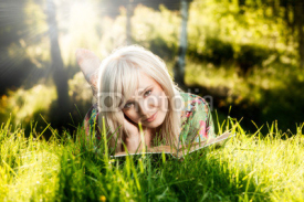 Young girl lies on green grass and reads book