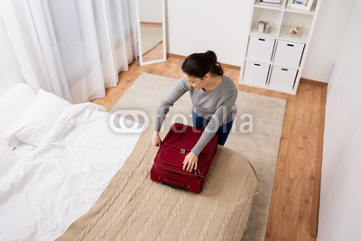 woman packing travel bag at home or hotel room