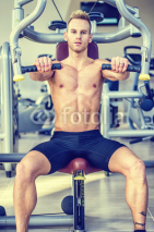 Muscular, shirtless young man in gym exercising pecs on pectoral machine