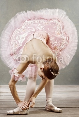 Young dancer in beautiful tutu fixing her slippers