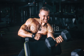 power athletic guy bodybuilder, execute exercise with dumbbells, in dark gym