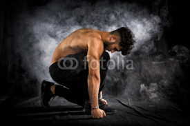 Handsome shirtless muscular young man kneeling down on black