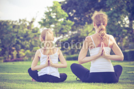 Obrazy i plakaty Mother and daughter doing yoga exercises on grass in the park.