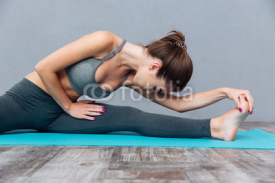 Young fitness woman doing splits isolated on grey background