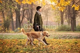 Naklejki A girl and her dog walking in a park in autumn