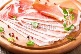 Naklejki sliced prosciutto ham on chopping board with oregano and pepper