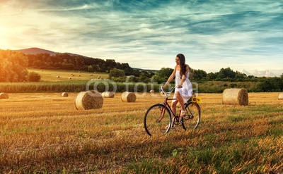 Beautiful woman cycling on an old red bike, in a wheat field