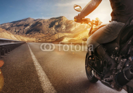 Naklejki Biker riding motorcycle on an empty road at sunset