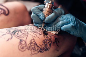 Naklejki Closeup tattoo artist fill circuit tattoo in a professional salon. Leg with a pattern and black paint. Master works in black sterile gloves. 