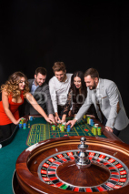 Group of young people behind roulette table on black background