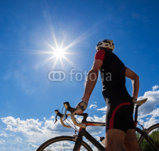 Obrazy i plakaty Road cyclist resting on his bike. Backlight, sunny summer day.