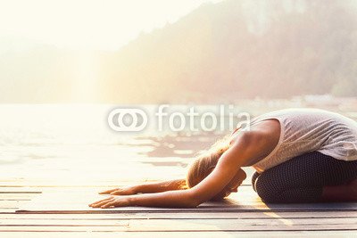 Sun salutation yoga. Young woman doing yoga by the lake, bathing in sunlight.
