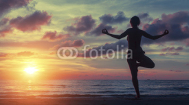 Obrazy i plakaty Yoga woman exercising on the beach during a stunning sunset. Peace, harmony, health and meditation.