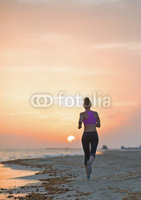Fitness young woman running on beach in the evening . rear view