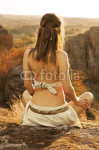 Primitive woman sitting on a rock at the sunset. Amazon woman