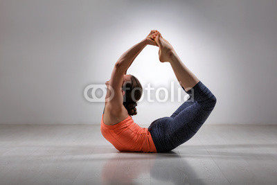 Sporty fit woman practices yoga asana Dhanurasana