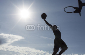 Fototapety Basketball player silhouette slam dunking on a sunny day