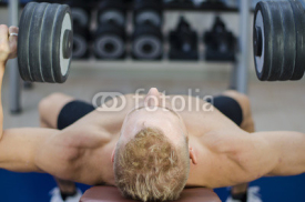 Muscular young man shirtless, lifting dumbbells training pecs on gym bench