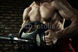 Sports background. Closeup photo of handsome bodybuilder guy prepare to do exercises with barbell in a gym, keep barbell plate in hands