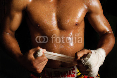 The muscular fighter tying tape around his hand preparing to