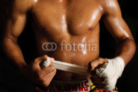 Naklejki The muscular fighter tying tape around his hand preparing to