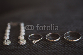 wedding rings and engagement ring and long earrings on dark textured background