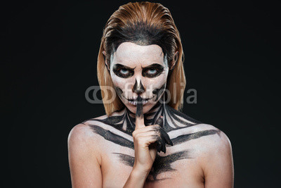 Portrait of woman with gothic skeleton makeup showing silence gesture