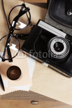 Obrazy i plakaty Retro camera on table with glasses and sheets of paper