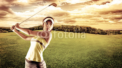 Young female golf player swinging with golf club outdoors