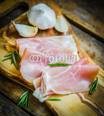 Prosciutto with garlic and rosemary on rustic wooden background