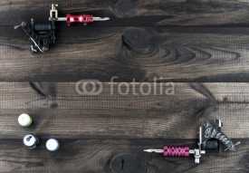 Fototapety Tattoo machines and three bottles of ink isolated on wooden background. Tattoo guns.