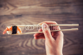 Fototapety Hand holding sushi roll using chopsticks
