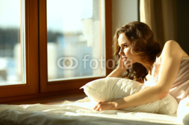 Woman lying in bed at early morning near window