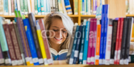 Naklejki Smiling female student reading book in the library