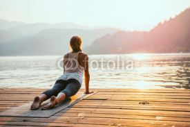 Naklejki Yoga sun salute. Young woman doing yoga by the lake at sunset