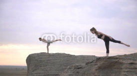The girl and the guy together doing yoga on the rocks