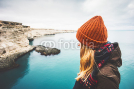 Young Woman enjoying cold sea view alone Travel Lifestyle concept adventure vacations outdoor. Blonde girl wearing fashion orange knitted hat and scarf. Melancholy solitude emotions