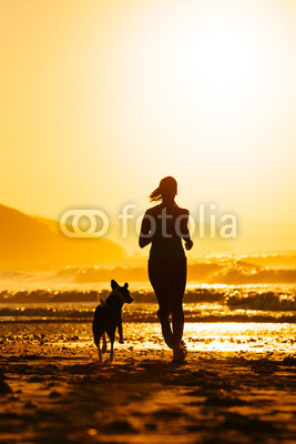 Woman and dog running on beach at sunrise