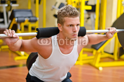 Handsome young man doing squats in gym