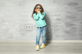 Cute little African American girl with sunglasses against grey wall. Fashion concept
