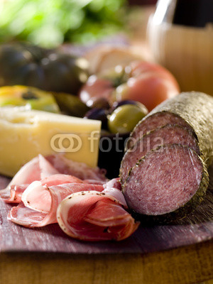 Rustic wood platter with meat, cheese and vegetables.