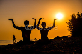 Fototapety An attractive young woman and man doing yoga on the beach, Sea